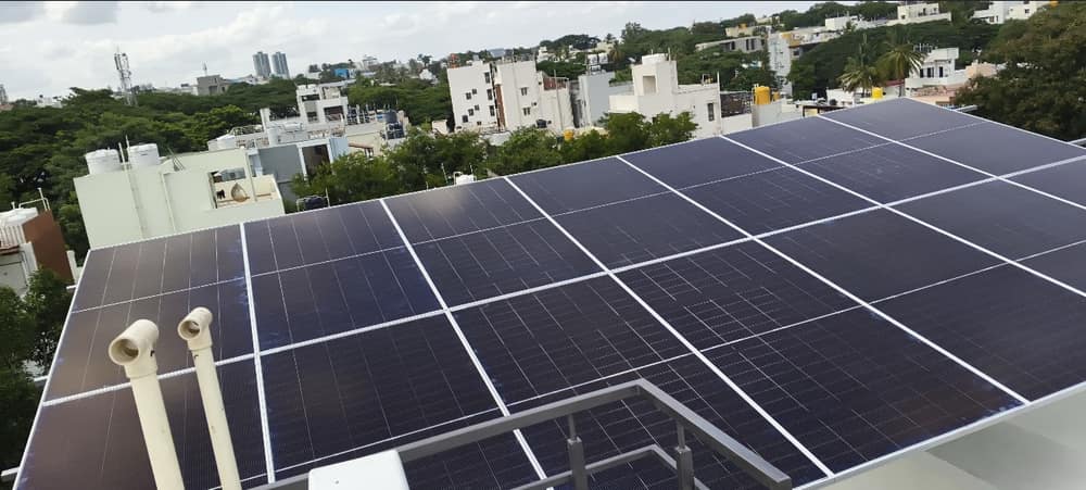 Rooftop solar array across a residential terrace in Bengaluru, with the city skyline behind
